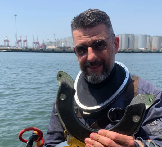 Man holding a yellow diving suit with a harbor in the background wearing Maskoptix glasses