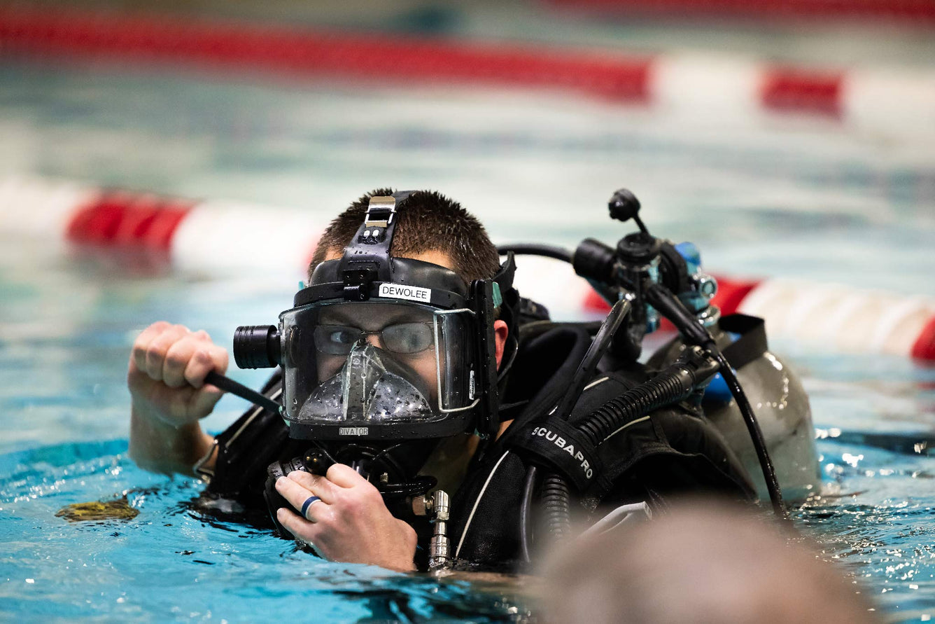 Person in scuba gear swimming in a pool with underwater camera equipment.