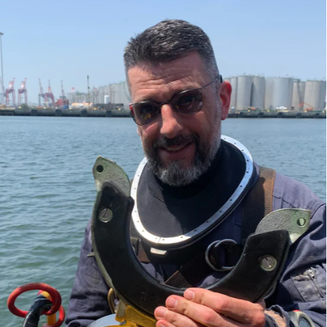 Man holding a yellow diving suit with a harbor in the background wearing Maskoptix glasses