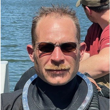 Person wearing a scuba diving suit with water in the background