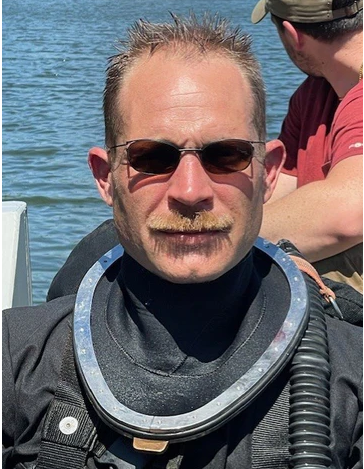 Person wearing a scuba diving suit with water in the background